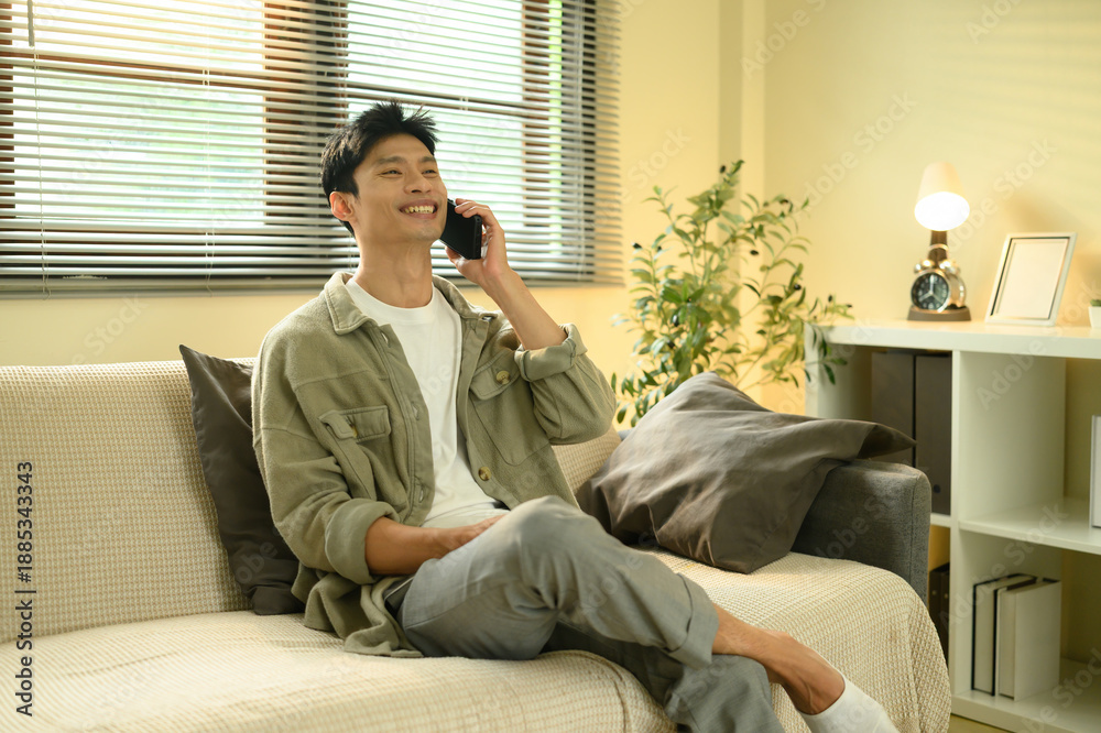 Fototapeta premium Smiling man using his mobile phone while relaxing on a couch in a modern and peaceful living space