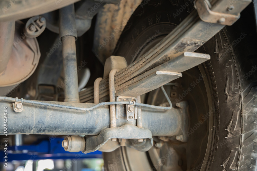 Fototapeta premium Close-up of rusty car rear differential axle housing and leaf spring suspension undercarriage view in auto repair garage, Drive shaft, Oil change, Mechanic workshop, Heavy duty vehicle