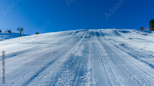 Groomed ski slope captured at an angle, showing textured snow surface and ski tracks, ideal for alpine sports, winter tourism, and resort marketing visuals