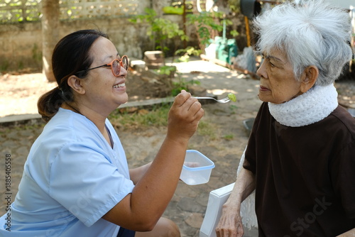 The caregiver is feeding the elderly person.