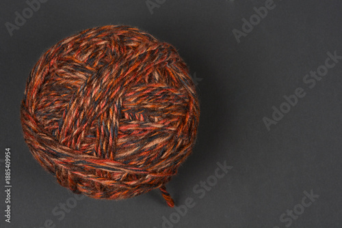 A top view of a single round ball of variegated brown and orange wool yarn placed on a dark grey surface with copy space