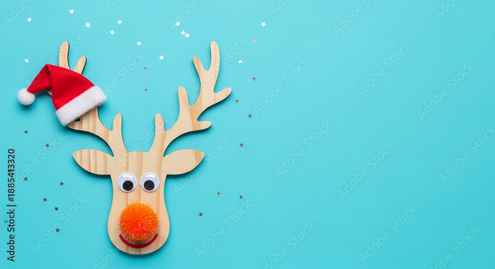 Naklejka premium Wooden reindeer with a red hat on turquoise background with small stars, showing the spirit of Christmas, winter holiday and festive mood for decoration