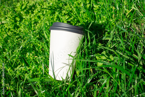 Discarded paper cup lying on green grass as  pollution concept