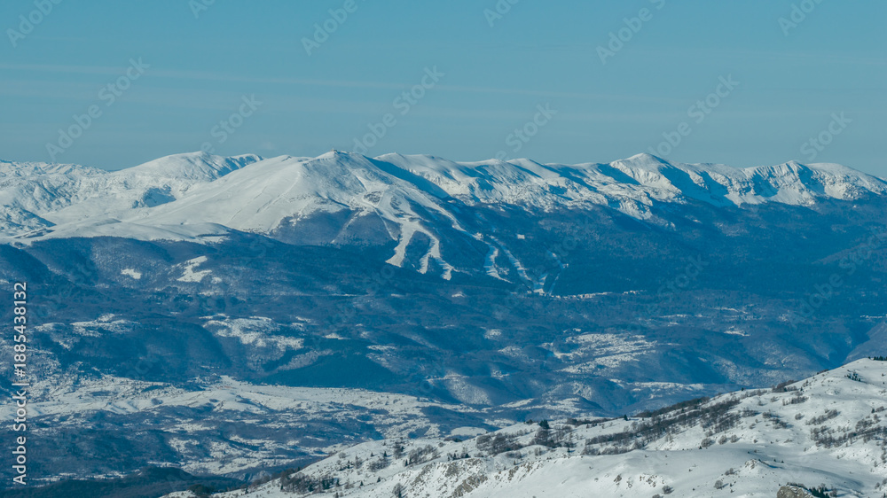 Obraz premium Distant view of Bjelašnica mountain with visible ski slopes and winter terrain, illustrating alpine skiing infrastructure within a rugged mountain environment