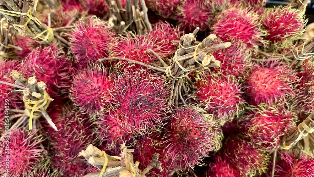 Obraz premium Fresh red rambutan fruits with stems in a local tropical market.