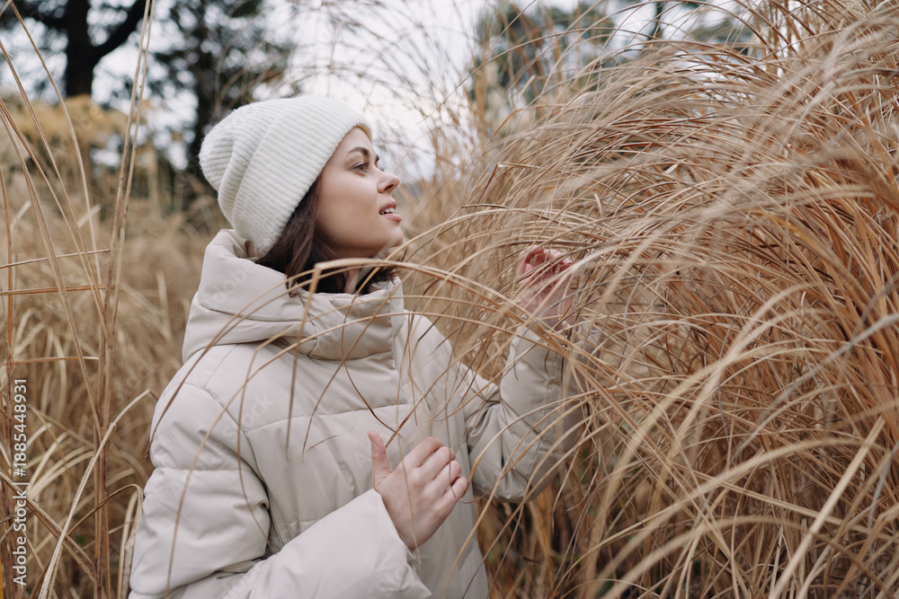 Fototapeta premium woman winter coat beanie grass field outdoor nature, serene portrait of a thoughtful model in soft neutral tones, capturing quiet solitude among tall grasses during a chilly day, exploration of calm