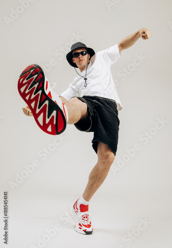 Full body shot of a stylish male dancer performing dynamic moves. Low angle wide-angle perspective emphasizes motion, energy and modern street dance style in studio.