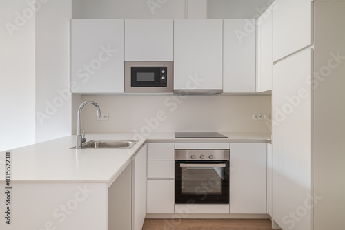 Modern kitchen with white cabinets, stainless steel appliances, and a minimalist design. Features a sink, microwave, and oven.