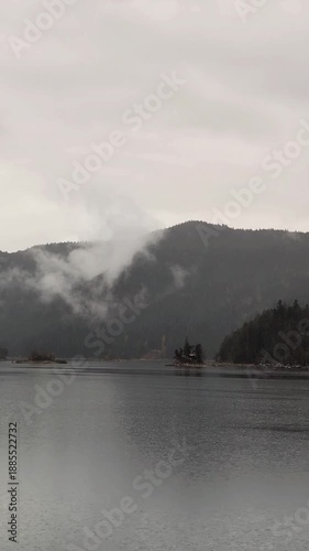 A wide horizontal shot of a calm mountain lake during rainfall.