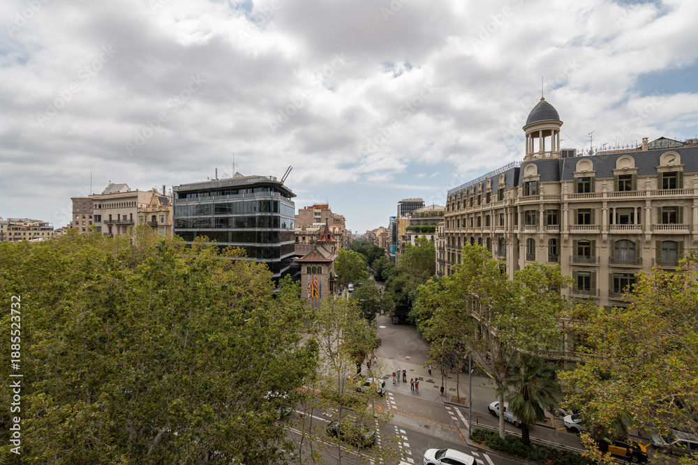custom made wallpaper toronto digitalUrban landscape of Barcelona Eixample district featuring a mix of modern and historical architecture. Green trees line the street under a cloudy sky. Cars are parked along the road.