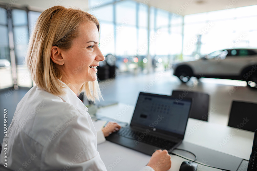 Obraz premium Smiling saleswoman working in car dealership showing new vehicles