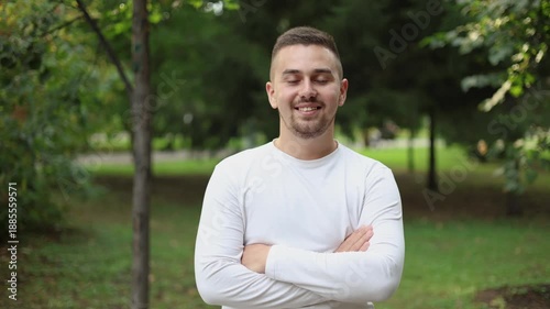 Portrait of a young man. The man smiles while standing against the backdrop of a green park.