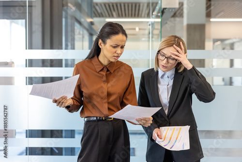 Φωτογραφία Two diverse businesswomen reviewing documents with concerned and frustrated expr