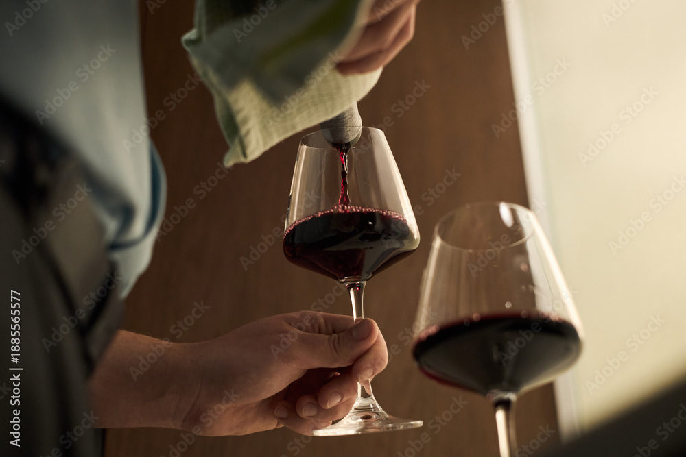 custom made wallpaper toronto digitalCaucasian middle aged man pouring red wine into glass, holding stemware with one hand while using towel to steady bottle, close up of hands and wine glasses in indoor setting