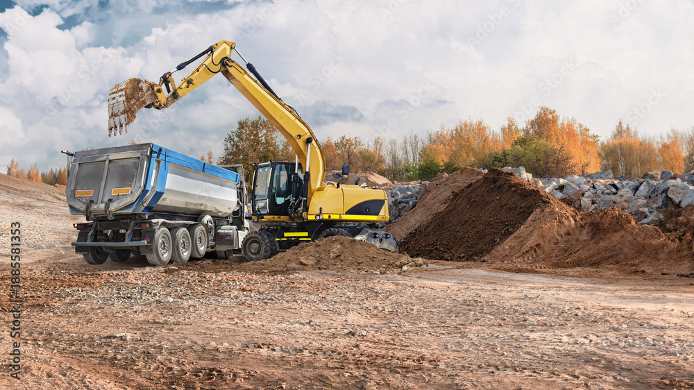 Obraz premium Construction workers use a loader and excavator to move dirt and materials at a site with trees and rocks in the background during daytime