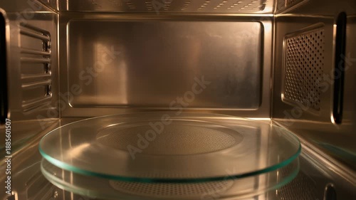 Interior view of a metallic, illuminated oven featuring a glass plate. Grid and ventilation detailing. Reflections and symmetry create an interesting perspective