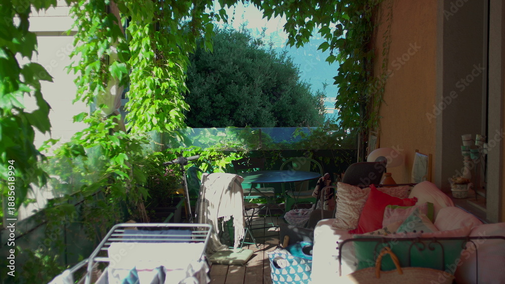 Naklejka premium Shaded garden balcony with cozy furniture, climbing plants, drying rack and mountain view in background, peaceful domestic outdoor space on sunny summer day