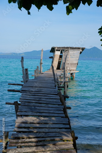 Foto Rustic wooden pier leading to toilet hut over turquoise sea