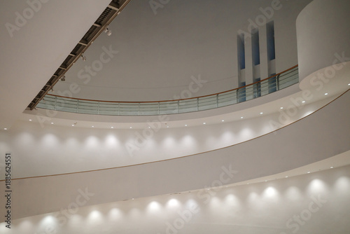 Slika na platnu A minimalist interior view of an architectural space featuring smooth, spiraling white walls illuminated by recessed spotlighting along a curved walkway and a balcony with a glass railing