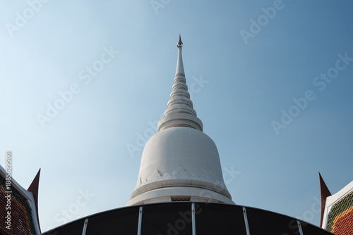 Obraz na płótnie A low-angle view of a traditional white Thai-style stupa (chedi) at a temple, showing the architectural detail of the spire reaching into a clear sky during the day