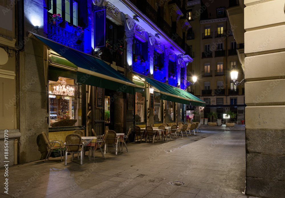 Fototapeta premium Cozy old street with table of restaurant in Madrid, Spain. Architecture and landmark of Madrid. Night cityscape of Madrid.