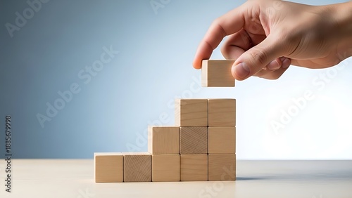 Hand building a staircase with wooden blocks on a table
