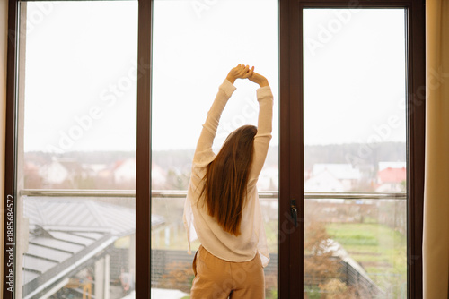 фотографія Woman stretching in a bright room while looking out at a cloudy landscape in the