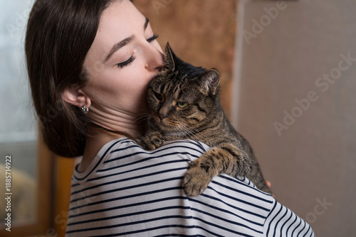 Close-up of a young caucasian woman hugging and kissing a cute, friendly, fluffy domestic cat. Pet, animal.