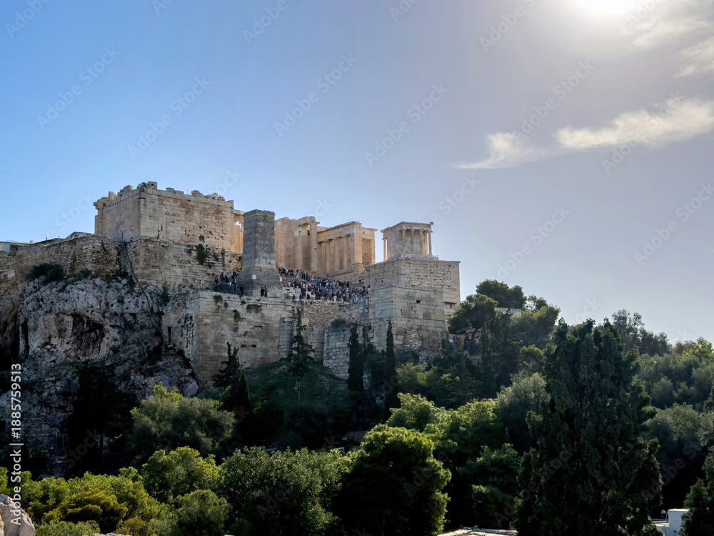 Obraz premium Acropolis of Athens and propylaea gate, visitors on the ruins, green trees, blue sky, view from Areopagus hill, Greece.