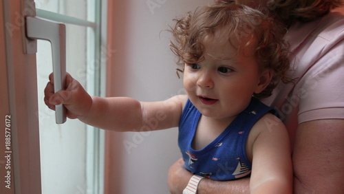Fotografia Curly-haired toddler held by grandmother reaches to touch door handle while look