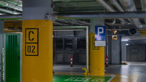 Underground parking with yellow and green coating. Underground parking with a pile of pipes on the ceiling and a parking sign