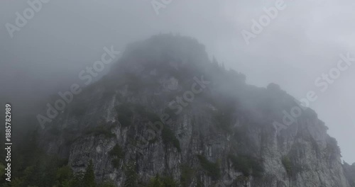 Slow aerial climb over a large rock cliff in thick fog