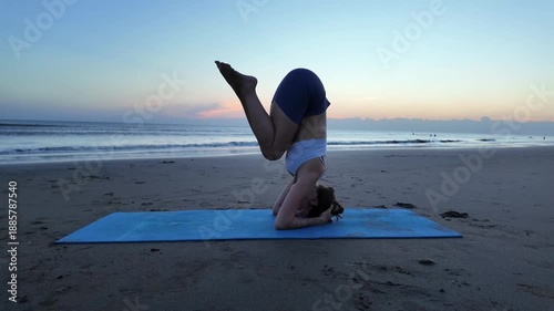 Silhouette of lesbian woman practicing yoga headstand on beach at sunset