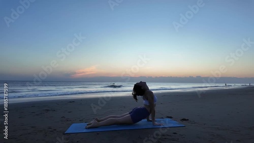 Lesbian woman performing sun salutation yoga on the beach at sunrise