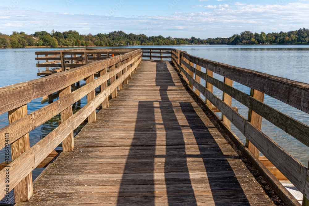 Obraz premium Serene Midday Walkway Extending Over Calm Water with Wood Dock and Shadows