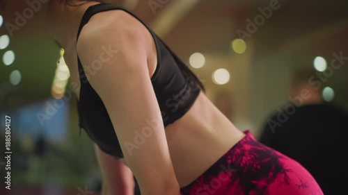 asian woman doing bent over row, wearing bright pink patterned leggings, sports bra, precise hip hinge, dumbbell in hand, sweat glistening, mirrored weight racks and blurred gymgoers in background,