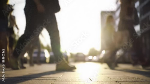 Low angle video of diverse pedestrians in casual clothes, legs in focus, walking on a vibrant, sun-drenched urban street with golden hour flare and creamy bokeh. Dynamic urban energy