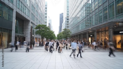 Vibrant city street scene captured with dynamic motion blur, depicting a bustling crowd of pedestrians moving between modern buildings, showcasing the fast pace of urban life