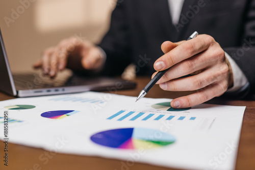 Wallpaper Mural Business professional analyzing financial reports with graphs and charts on a desk, laptop computer visible in the background, focused on data presentation Torontodigital.ca