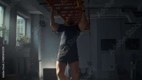Strong man in black activewear does pull ups on metal beam in gym