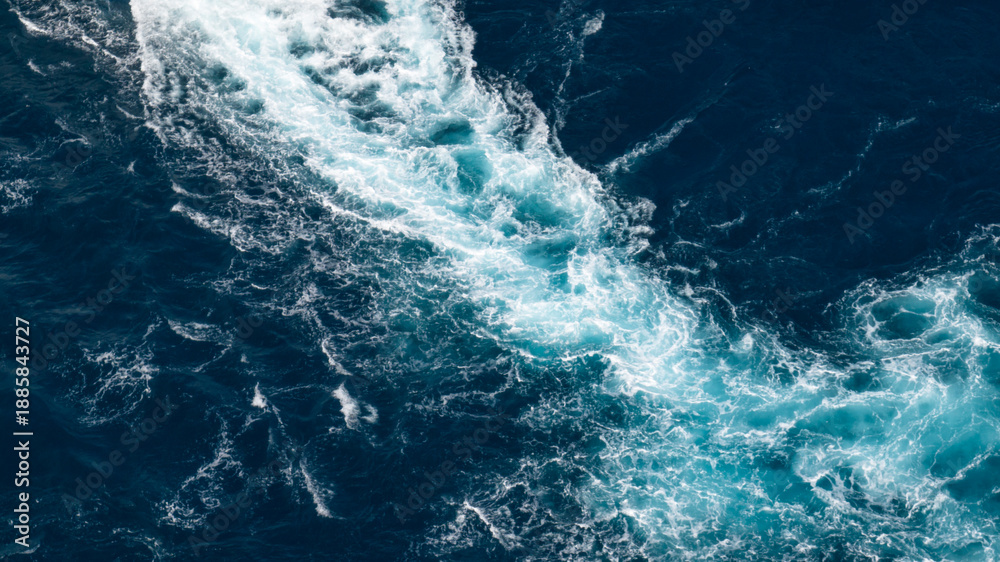 Obraz premium High-angle aerial close-up of a white foaming wake created by a vessel on the surface of the deep blue sea.