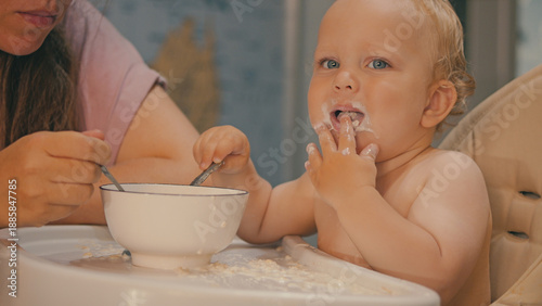 Photography A messy blue-eyed baby eats porridge with his hands while sitting in a high chair