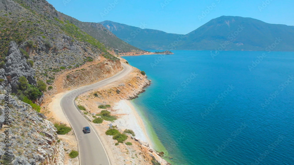 Obraz premium AERIAL: Grey car driving along the beautiful shoreline of a scenic remote island
