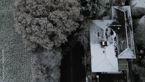 Overhead view of a snow-covered house and trees next to a dark road.