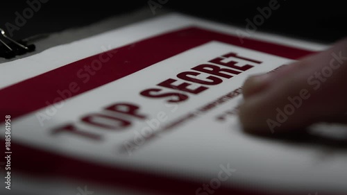 A paper folder of documents with a Top Secret cover page is handled under subdued lighting. Suggestive of spying, espionage, or cover-up.