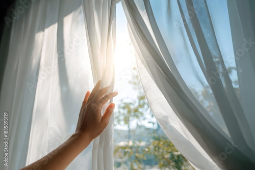 Hand opening sheer curtains to bright morning sunlight in airy home interior