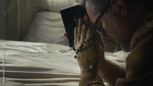 Close-up shot of devoted middle-aged man turning to God in prayer holding holy bible and rosary beads in folded hands