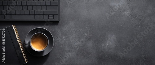 A dark, textured desk hosts a keyboard, notebook, and a cup of coffee. Modern workspace setup