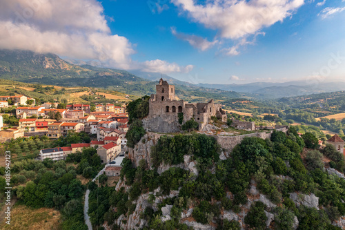 Aerial view of an ancient stone castle perched atop a rugged cliff, overlooking the quaint village, bathed in the soft glow of a sunny day, Quaglietta, Campania, Italy.