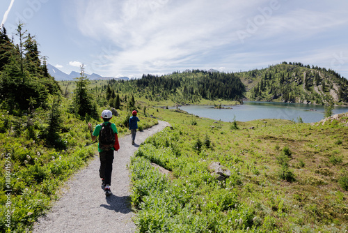 Two young boys walking along a trail in nature with a lake and green nature all around